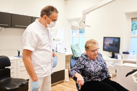 Oudere patiënt staat op uit de tandartsstoel